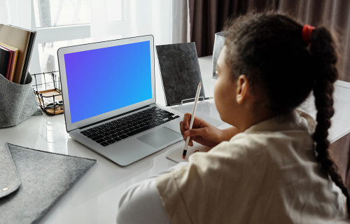 Young girl using a MacBook Air with a pencil and a jotter mockup